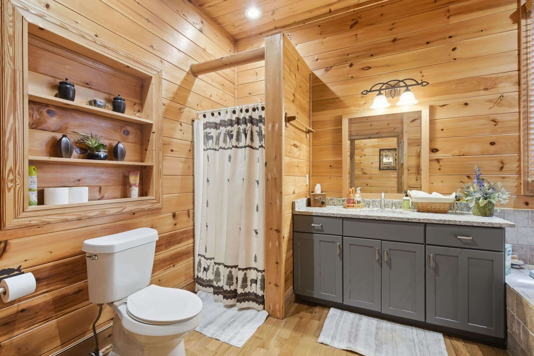 A wooden cabin bathroom with a toilet, shower curtain, vanity, and shelves with toiletries.