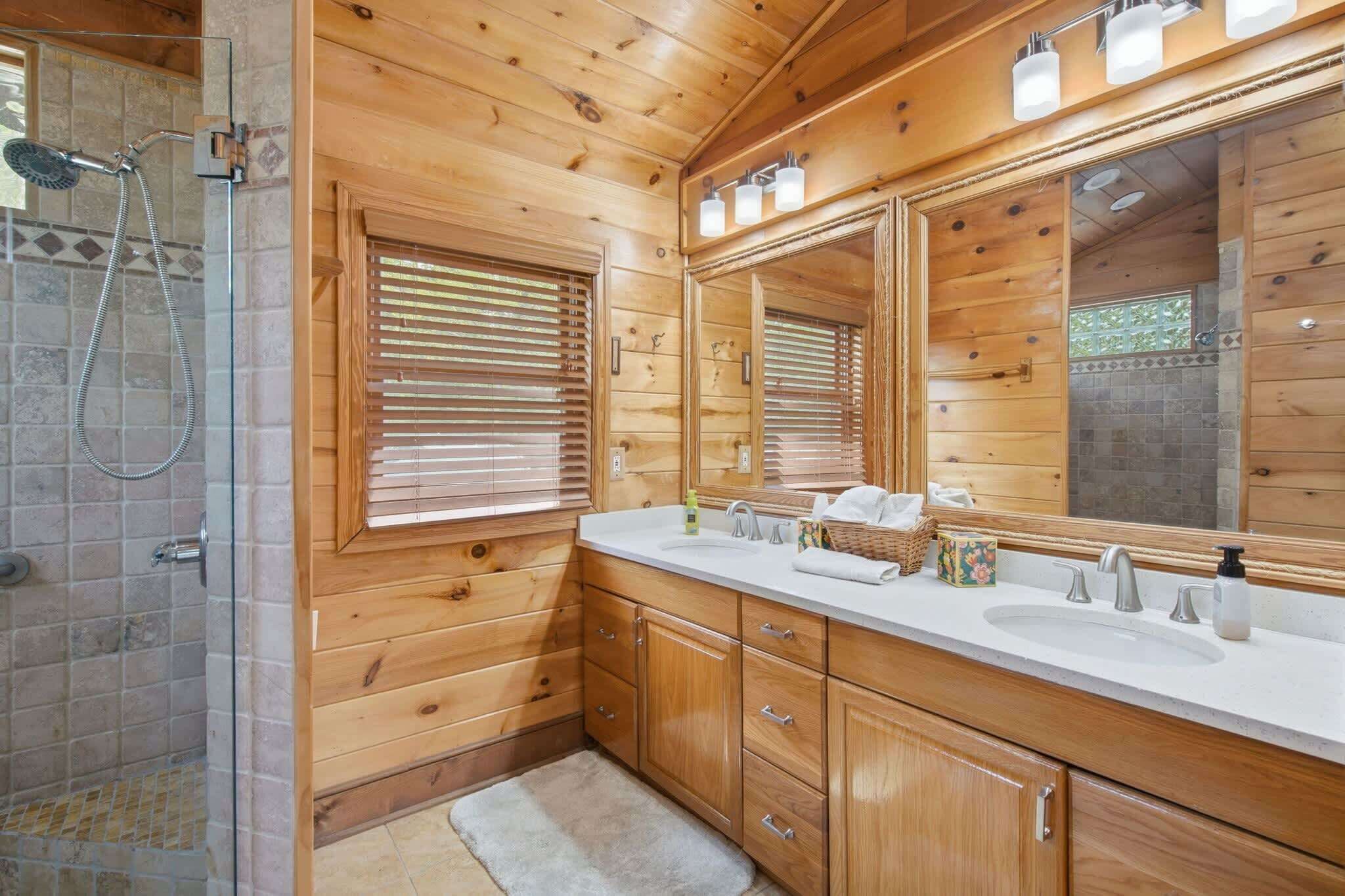 A wooden cabin bathroom with a shower, large mirror, wooden cabinets, and a white countertop.