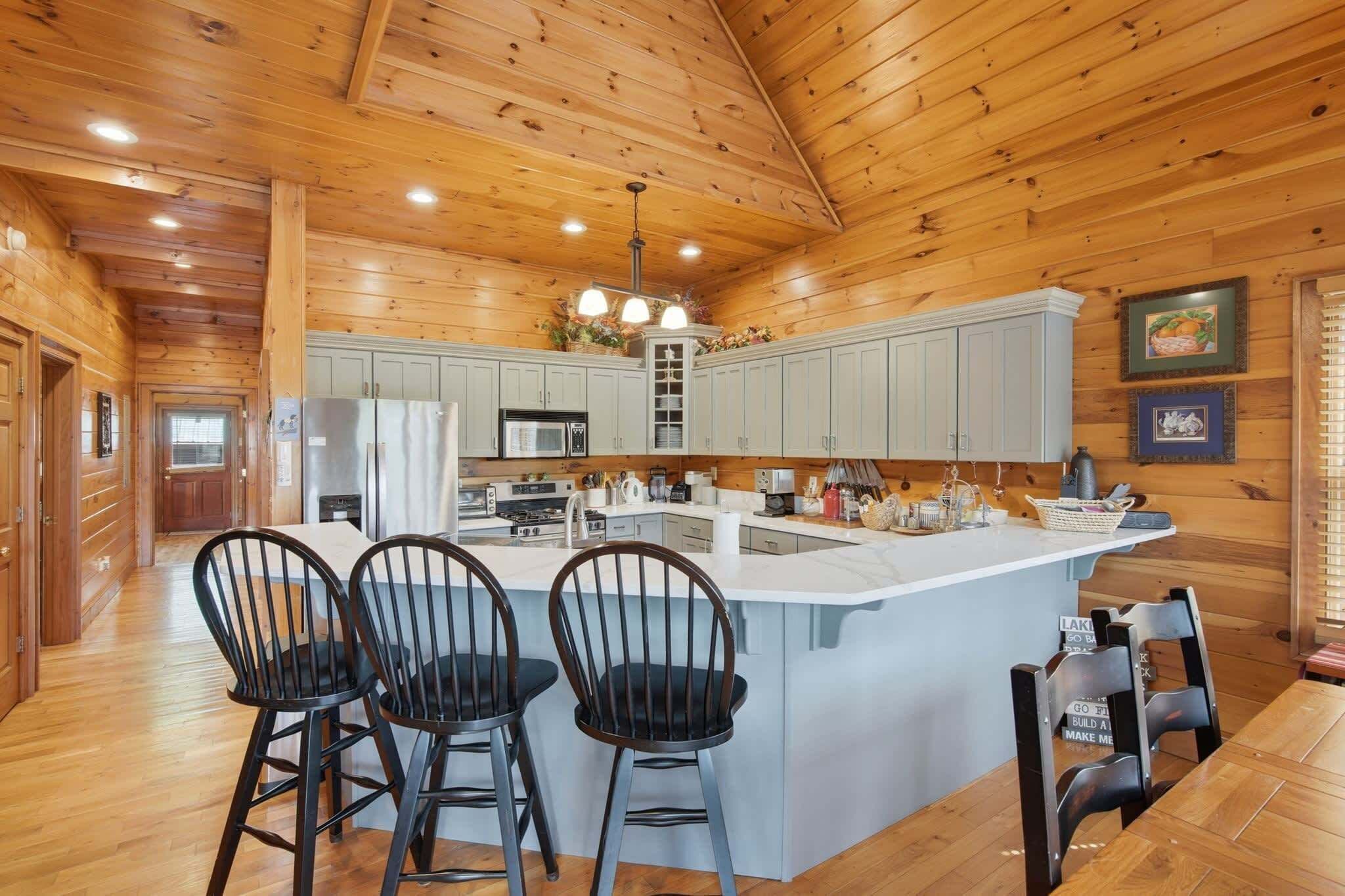 A wooden cabin interior with a kitchen island, bar stools, and a dining table.