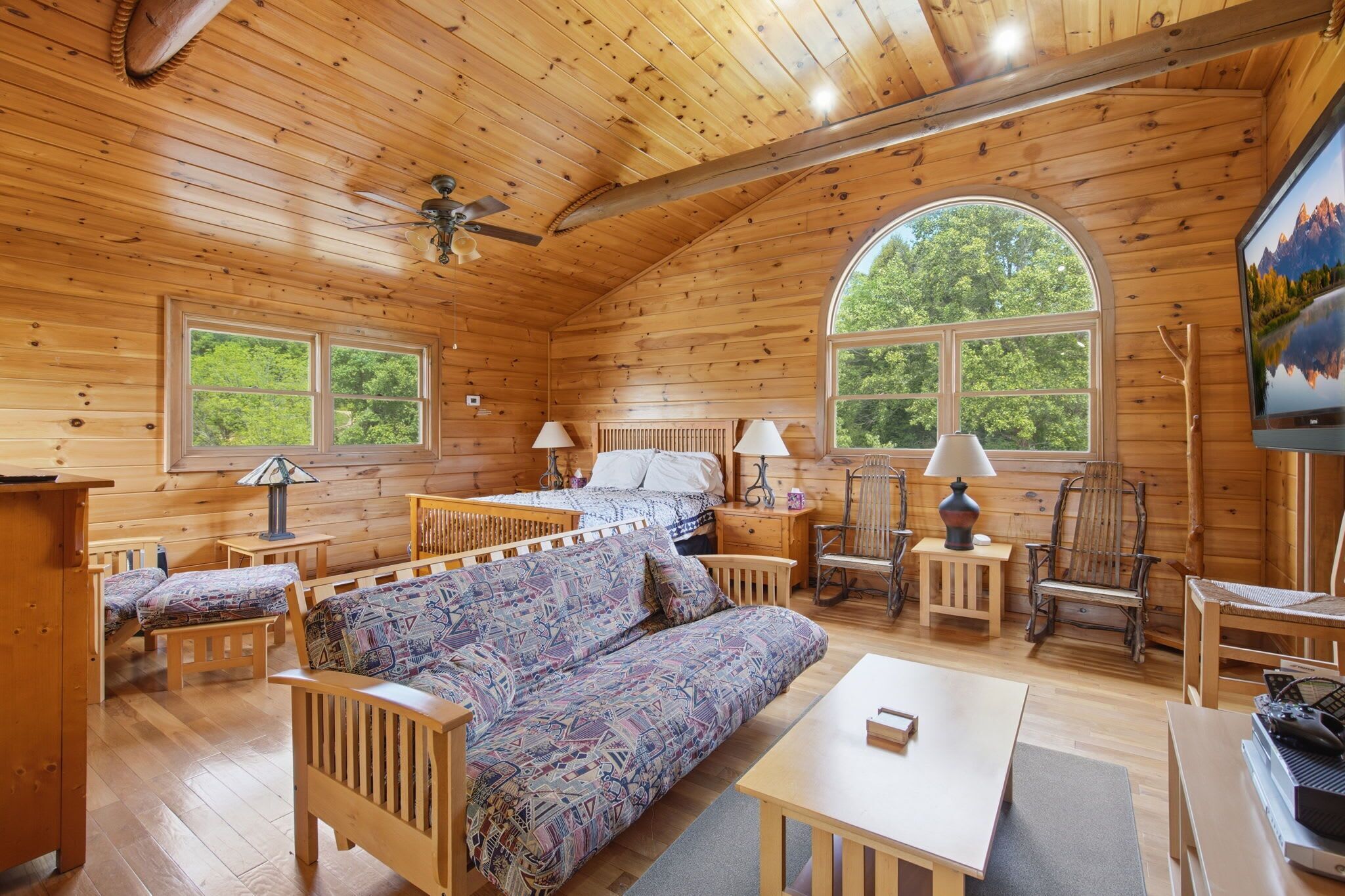 Une cabane en bois comprenant un lit, un canapé, des chaises, une table et un téléviseur.