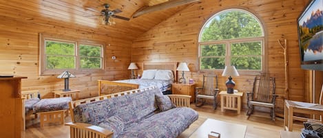 Une cabane en bois comprenant un lit, un canapé, des chaises, une table et un téléviseur.