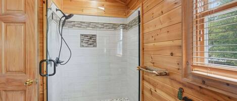 Une salle de bain rustique, avec des murs en bois, une douche en verre, des toilettes et une fenêtre équipée de stores.