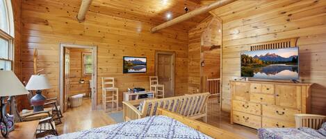 A wooden cabin interior with a bed, a TV, a desk, and a chair.