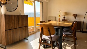 A dining area with a wooden table, chairs, a vase with flowers, a lamp, and a view of mountains through a window. - apart with terrace and unobstructed view (Nice)