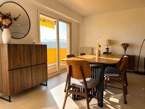 A dining area with a wooden table, chairs, a vase with flowers, a lamp, and a view of mountains through a window. - apart with terrace and unobstructed view (Nice)