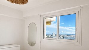 A bedroom with a bed, a dresser, a round mirror, and a window with a city view. - apart with terrace and unobstructed view (Nice)