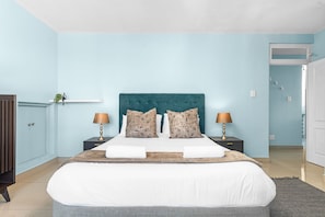 A bedroom with a large bed, two bedside tables with lamps, a wardrobe, and a door leading to another room. - Penvay Penthouse (Durban)