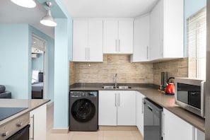 A compact kitchen with a washing machine, dishwasher, and microwave. - Penvay Penthouse (Durban)