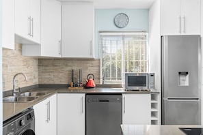 A modern kitchen with white cabinets, a stainless steel refrigerator, a dishwasher, a microwave, and a kettle. - Penvay Penthouse (Durban)