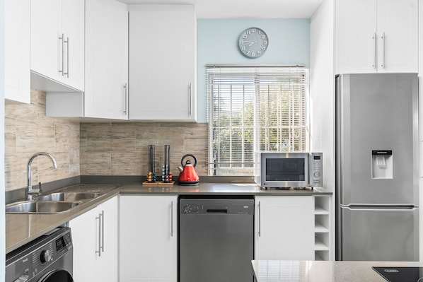 A modern kitchen with white cabinets, a stainless steel refrigerator, a dishwasher, a microwave, and a kettle. - Penvay Penthouse (Durban)