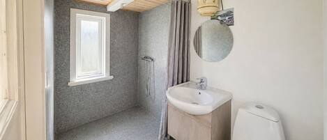 A bathroom with a shower, a sink, a toilet, a window, and a mirror.