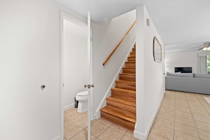 Eine Treppe führt zu einer zweiten Etage, eine weiße Tür, eine Toilette, ein graues Sofa und ein Deckenventilator.