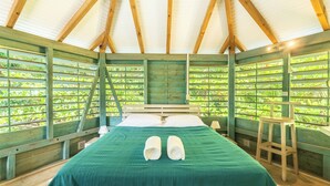 A room with a bed, green bedding, wooden beams, and a view of greenery through the window. - Bungalow Ixora, seaside (Les Anses-d'Arlet)