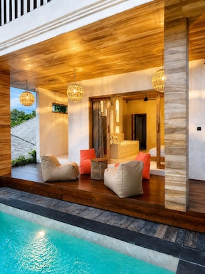 Zona junto a la piscina con suelo de madera, un área de descanso con cojines y vistas a la piscina.