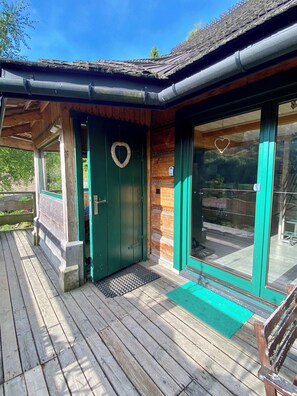 A wooden building with a green door, a window with a heart-shaped decoration, and a wooden deck.