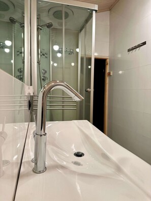 Un baño moderno con grifo de cromo, cabina de ducha de vidrio y lavabo blanco.