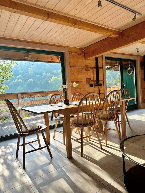 A wooden interior with a dining table and chairs, a view of the outdoors, and a green door.