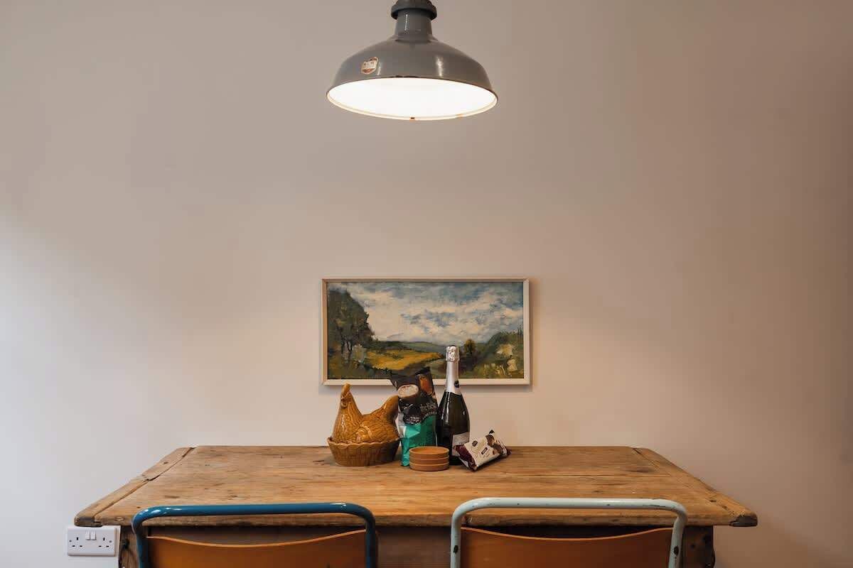 Een houten eettafel met stoelen, een schilderij aan de muur en een fles champagne.