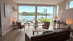 Ein geräumiges Wohnzimmer mit großem Fenster und Seeblick, einer Ledersofa und einem Essbereich mit Tisch und Stühlen.