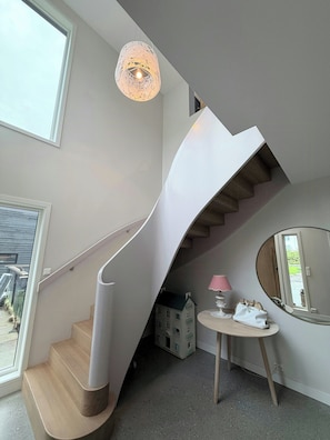 Ein modernes Interieur mit einer Wendeltreppe, einem runden Spiegel und einem kleinen Tisch mit einer Lampe.