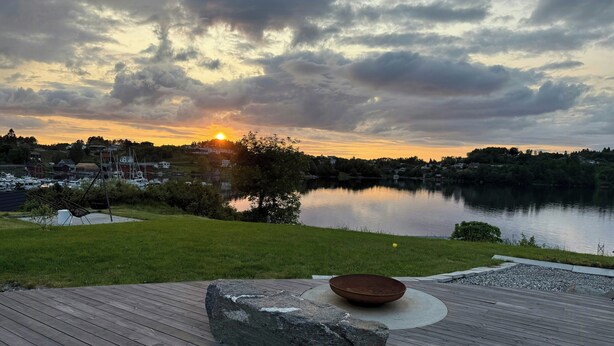 Eine Holzterrasse mit einem Stein und einer Schale, mit Blick auf einen See, im Hintergrund Boote und Häuser.