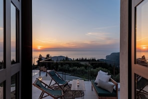 A balcony with a table, chairs, and a view of the sunset over a mountainous landscape. - Orion Sunset Villa (Erissos)