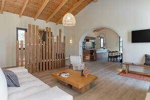 A spacious living area with a wooden ceiling, a sofa, a coffee table, and a TV mounted on the wall. - Orion Sunset Villa (Erissos)