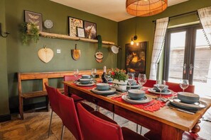 A dining area with a long wooden table set for six, red chairs, and a hanging light fixture. - Large farmhouse, heated pool, nr Chester, Parking (Holt)