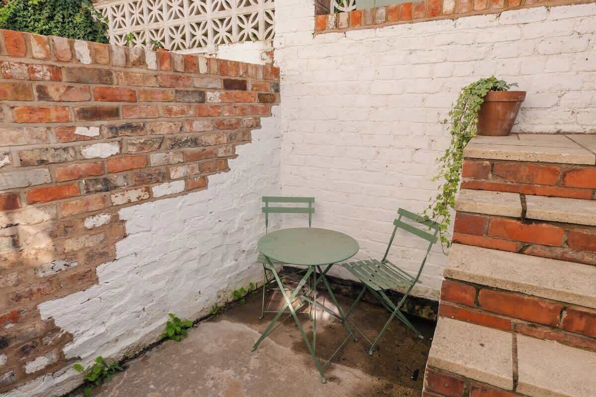 A small outdoor patio with a round table and two chairs, a brick wall, and a white fence.