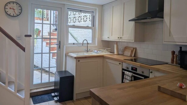 Una cocina moderna con armarios blancos, encimera de madera, campana extractora negra y ventana con vistas al exterior.