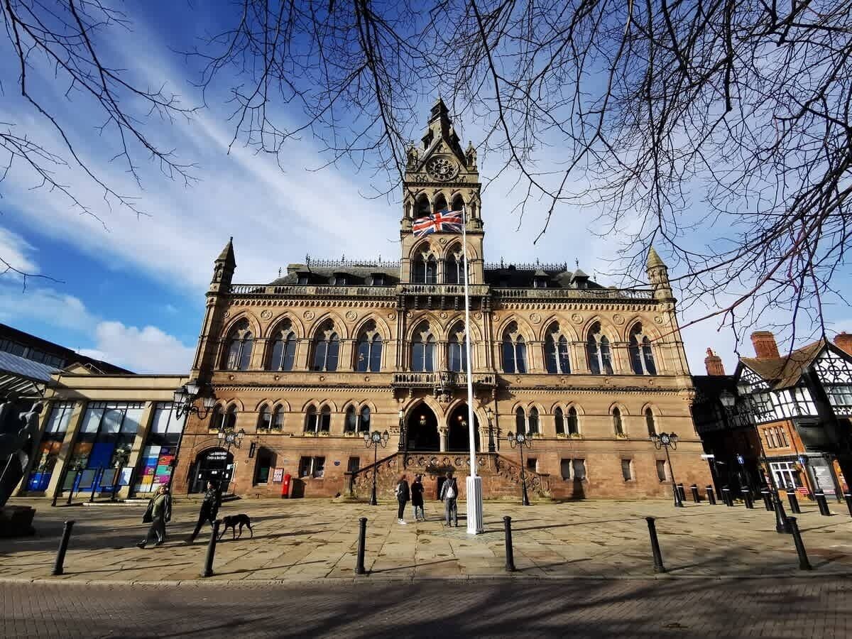 A historic building with a prominent clock tower, arched windows, and a flag.