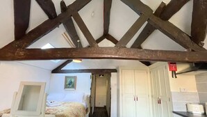 Une chambre avec un lit, une table de chevet, un miroir et une fenêtre. Un couloir mène à un coin cuisine équipé de placards et d’un grille-pain.