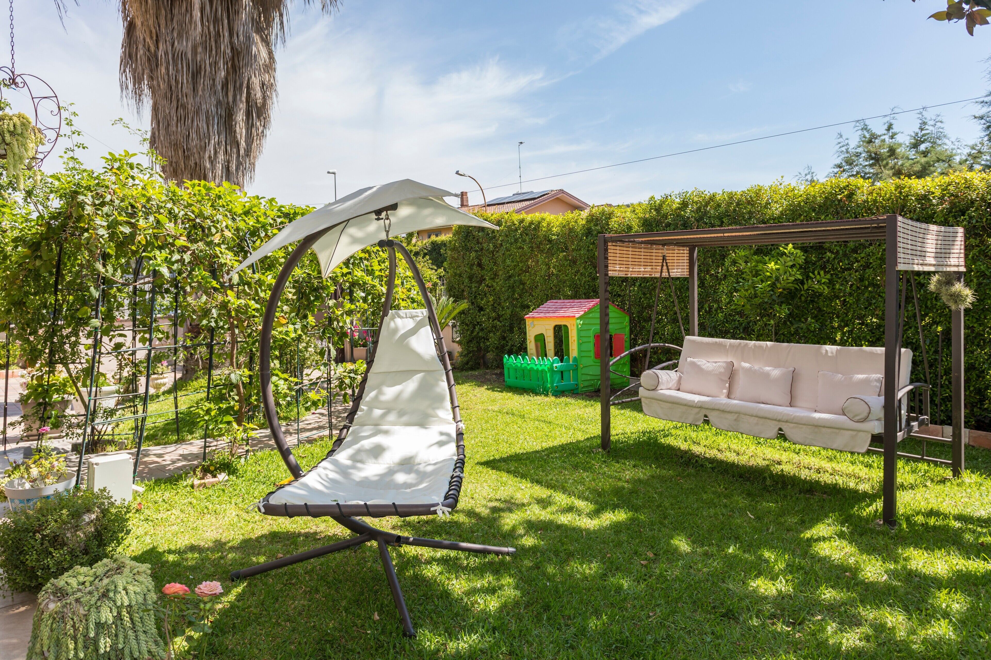 A garden with a swing, a white sofa, and a pergola.