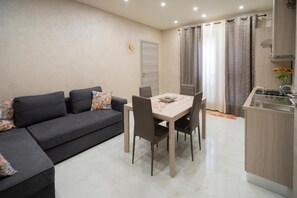 Ein modernes Wohnzimmer mit Sofa, Esstisch, Stühlen und einer Küchenzeile mit Herd.