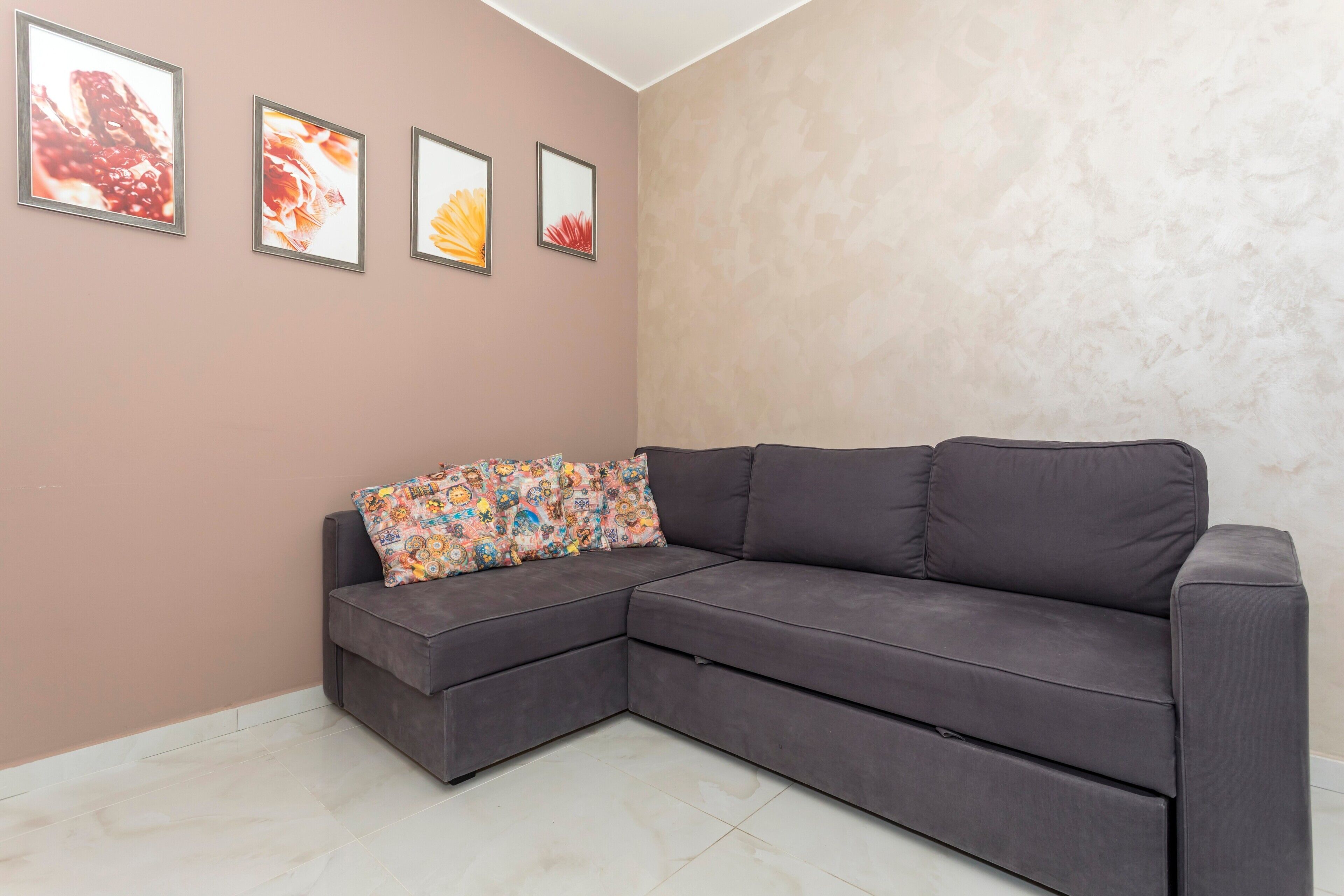 Ein Eckwohnzimmer mit einem grauen Ecksofa, einem farbenfrohen Kissen und vier gerahmten Bildern an der Wand.