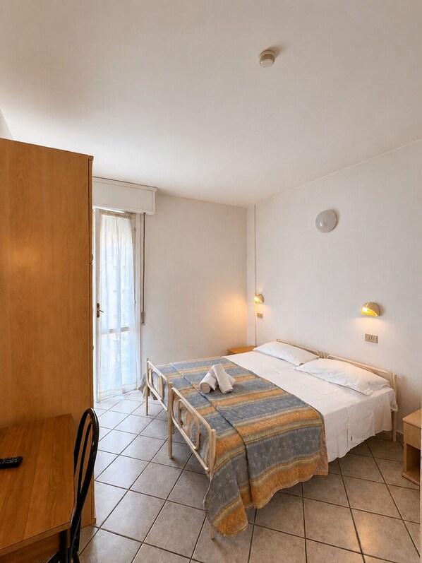 A single bed with a striped bedspread, a wooden wardrobe, a desk with a chair, and a door leading to an outdoor area. - Hotel Villa Isola (Rivazzurra)