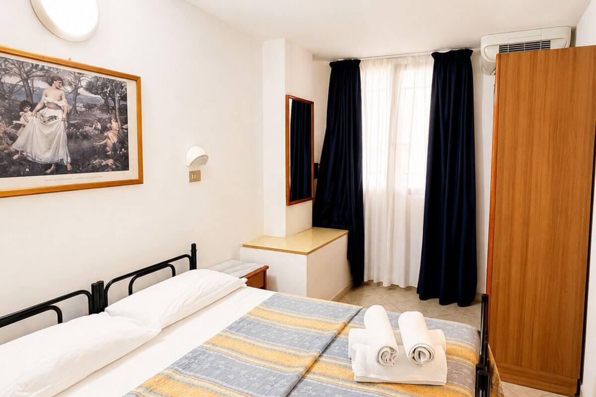 A hotel room with a bed, a bedside table, a mirror, a wardrobe, and a painting on the wall.
