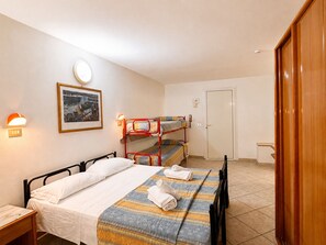 A room with bunk beds, a single bed, a bedside table, a wall-mounted lamp, a framed picture, and a door. - Hotel Villa Isola (Rivazzurra)