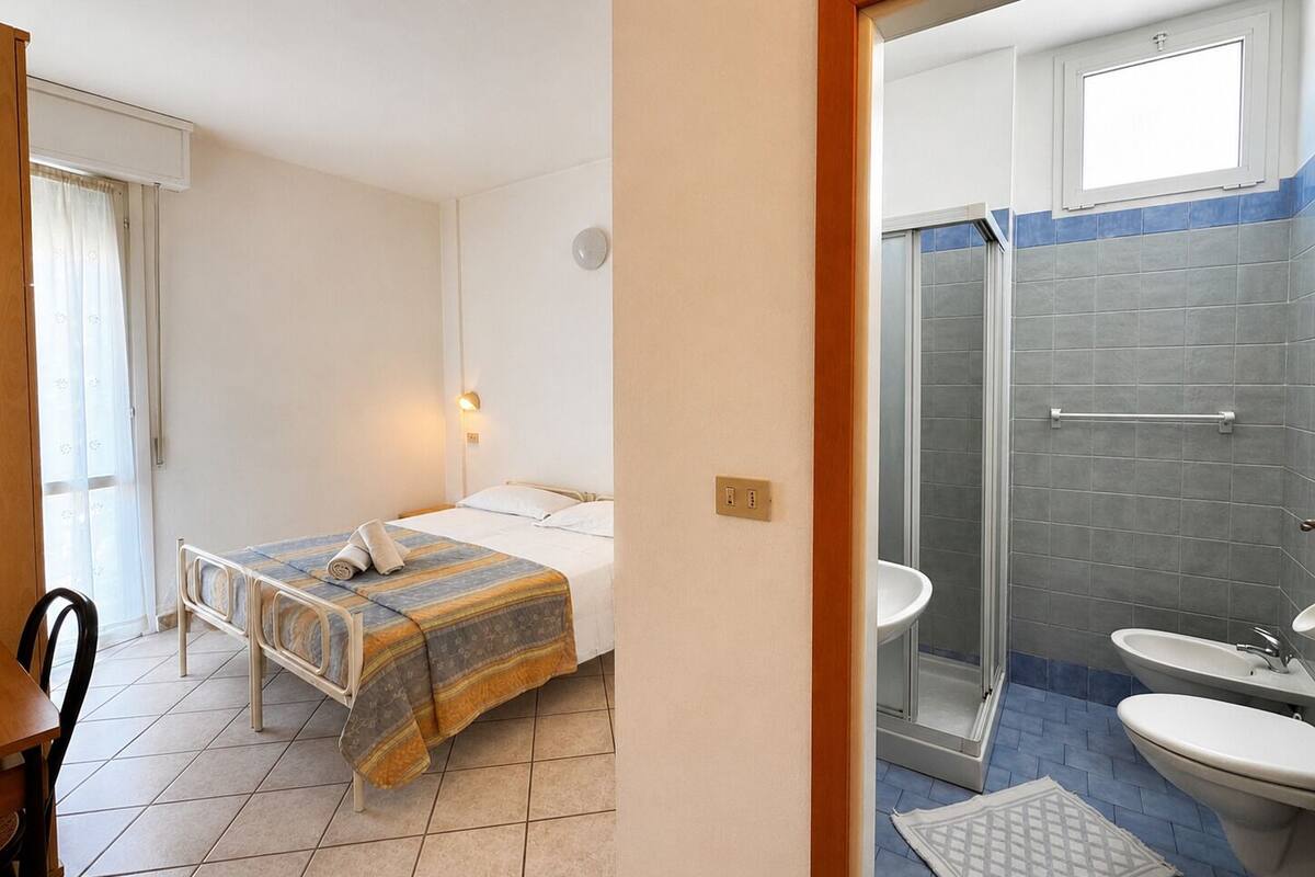 A hotel room with a bed, a bedside table, a chair, a bathroom with a shower, a sink, and a toilet.