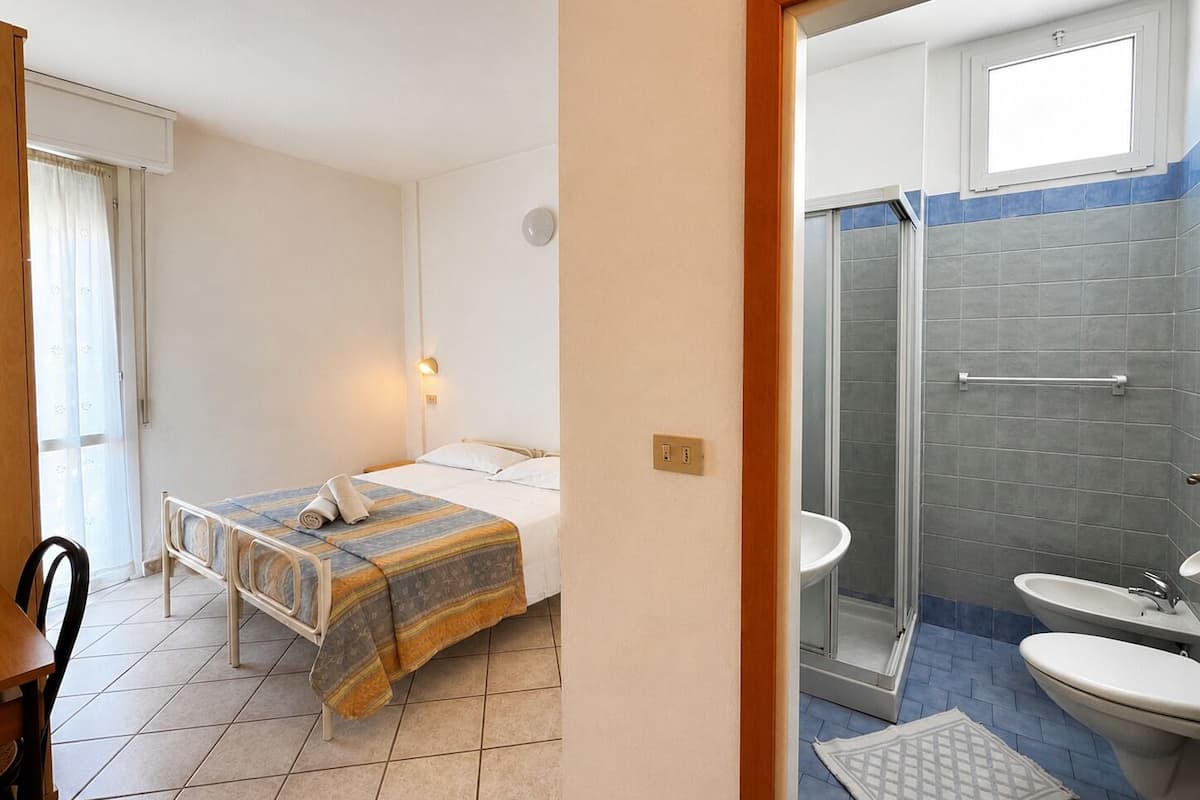 Hotellihuone, jossa on sänky, yöpöytä, tuoli sekä kylpyhuone, jossa on suihku, pesuallas ja wc.