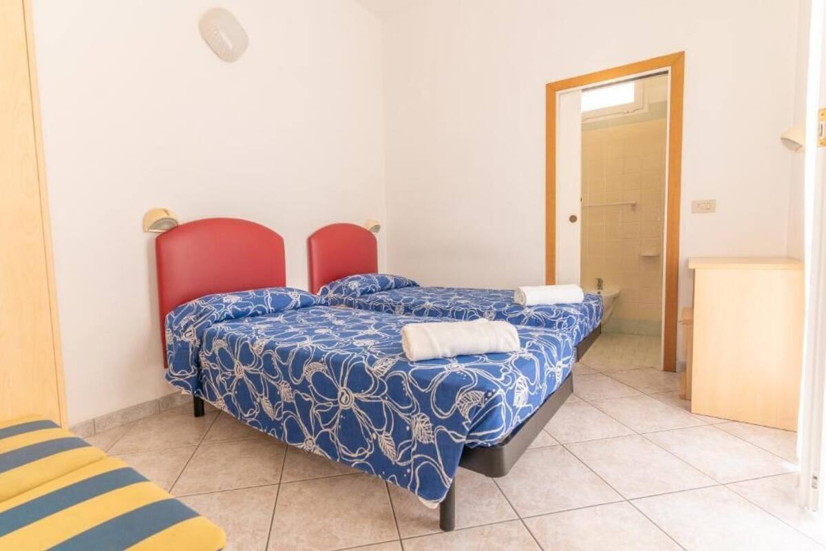 A double bed with floral bedding, a red headboard, and a small bedside table.