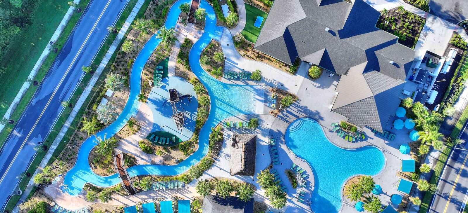 An aerial view of a resort with multiple swimming pools, a winding water feature, and a large building with a distinct roof pattern.