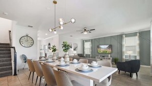Uma sala de jantar moderna com uma mesa comprida, cadeiras, um relógio e um ventilador de teto.