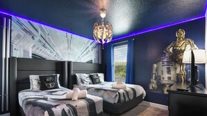 Quarto com duas camas, decoração inspirada em Star Wars, uma luminária no teto e janela com persianas.