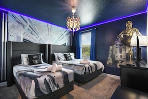 Ein Schlafzimmer mit zwei Betten, Star Wars-Dekoration, einer Deckenleuchte und einem Fenster mit Jalousien.