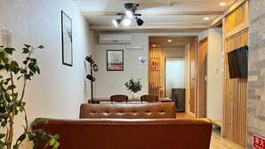 Un interior moderno con un sofá, piso de madera, ventilador de techo y televisor montado en la pared.