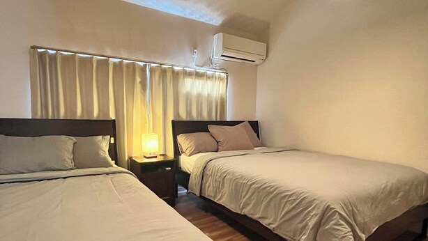 Habitación de hotel con dos camas, una mesita de noche, un equipo de aire acondicionado y una lámpara colgante.