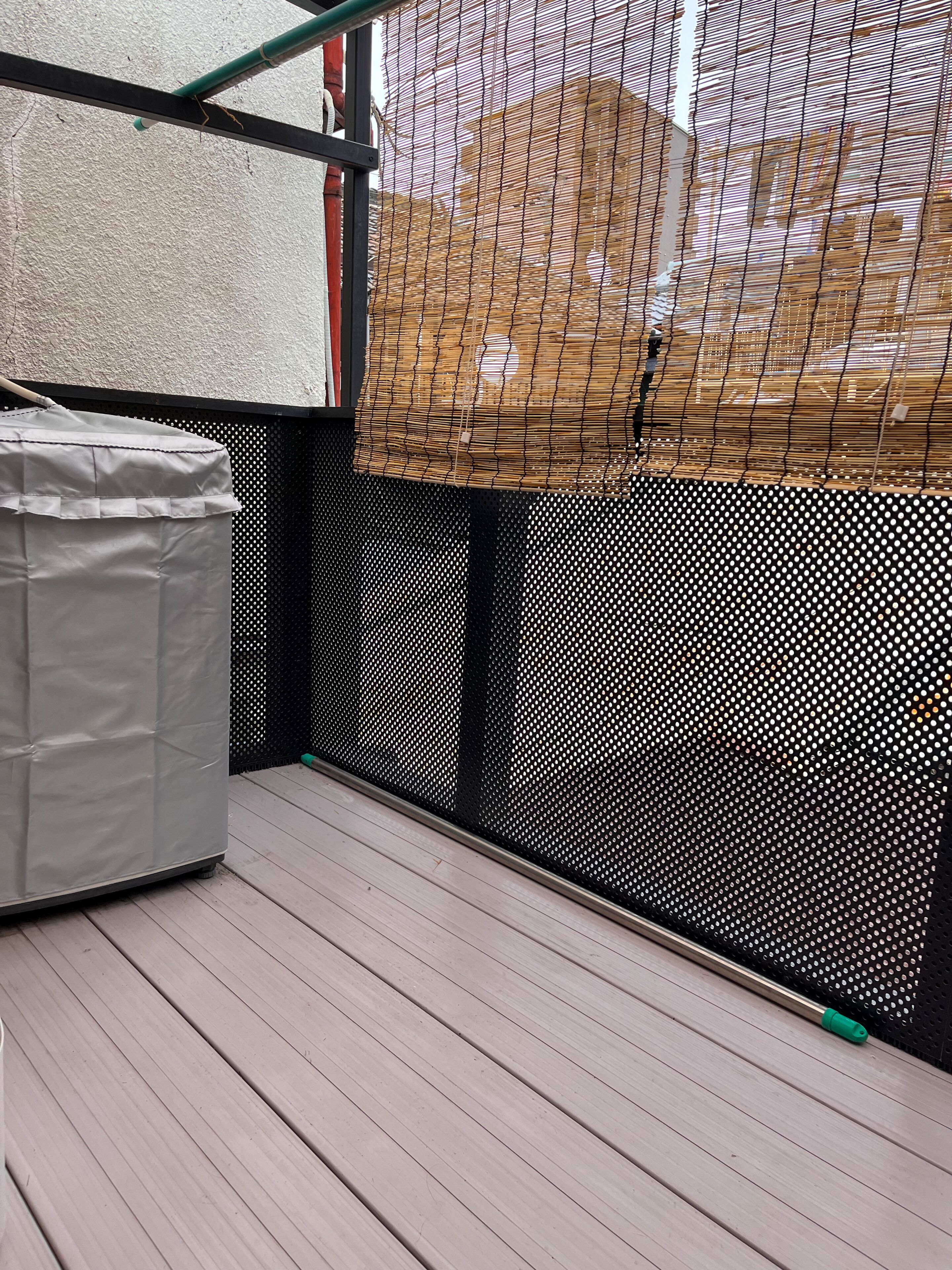 A room with a wooden deck, a white padded object, a black mesh screen, and a bamboo fence.