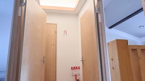 Un pasillo estrecho con puertas de madera, un tragaluz y un extintor.