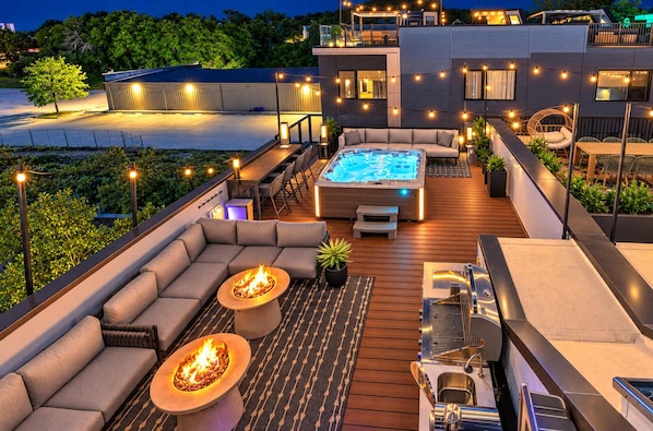 Une terrasse sur le toit avec un jacuzzi, des sièges d’extérieur et des guirlandes lumineuses.
